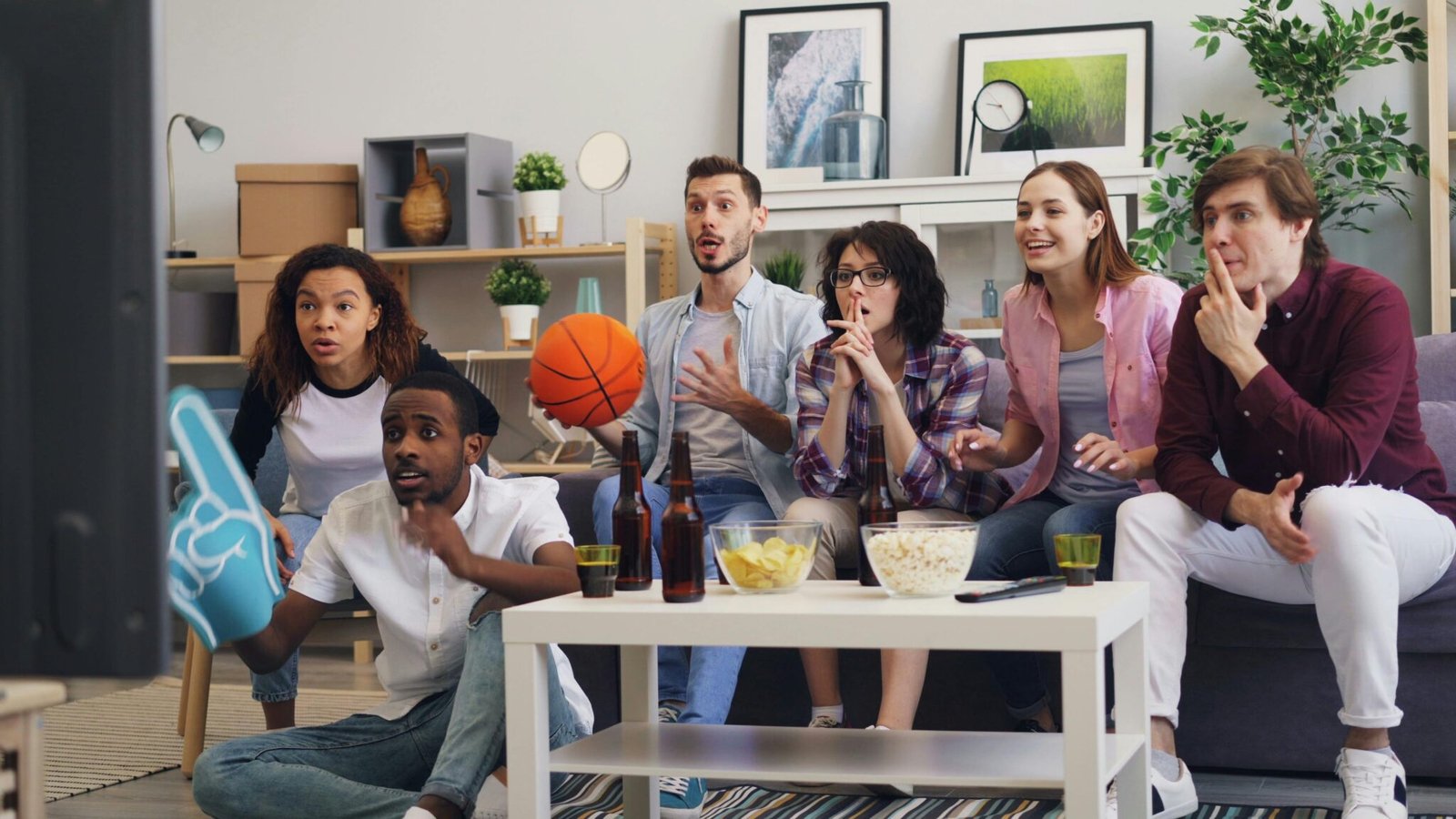 Group of friends excitedly watching a sports game indoors, enjoying snacks.